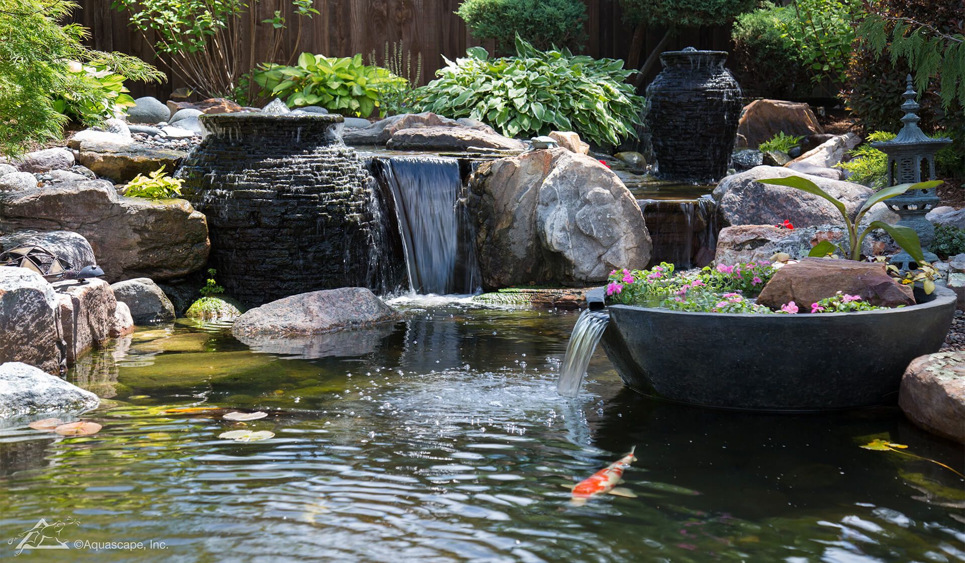 Koi pond with a waterfall running between stacked stone urns and planted rockwork
