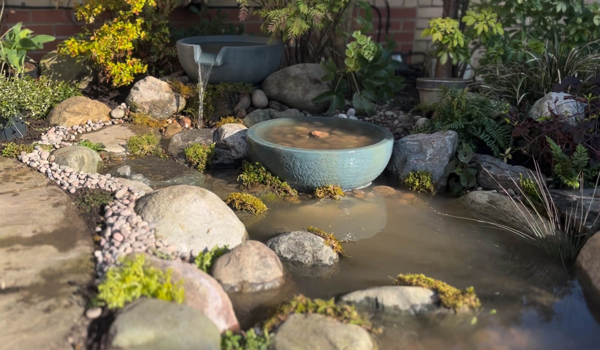 Ceramic bowl spilling into a shallow pebble stream edged with rounded boulders