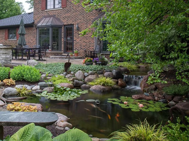 Koi pond with a small waterfall beside a brick house and patio