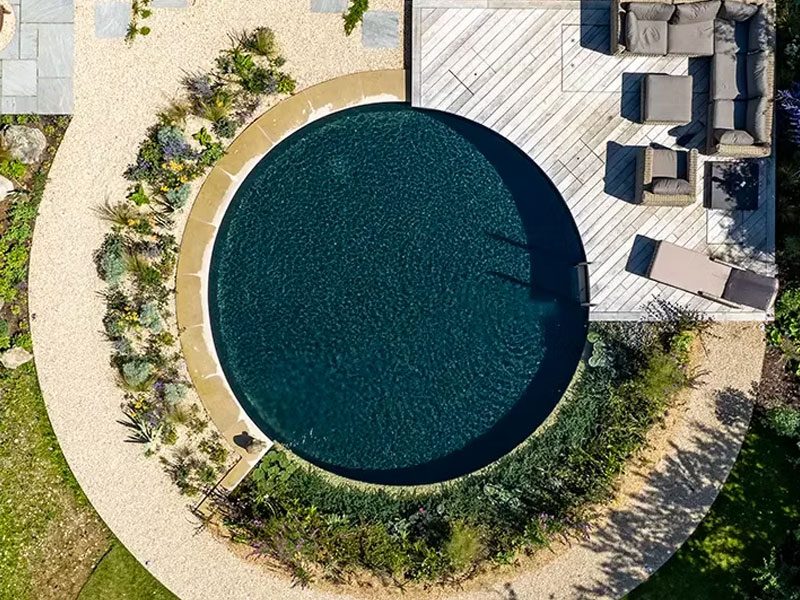 Circular swim pond set into a planted gravel garden beside a timber deck