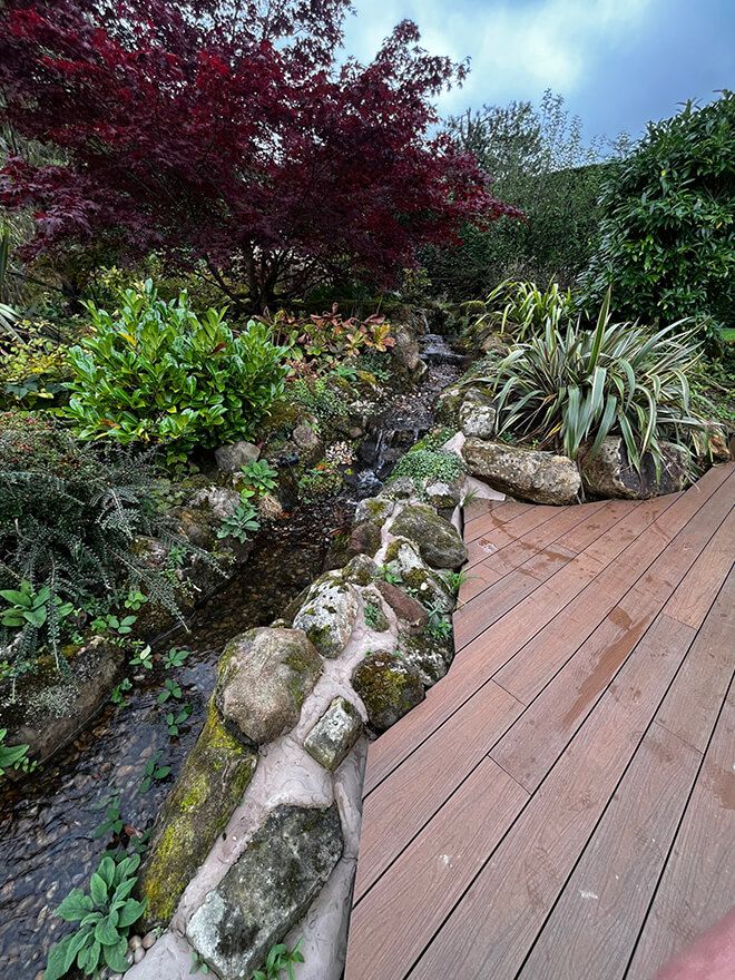 Rocky stream running alongside a hardwood deck under a red acer