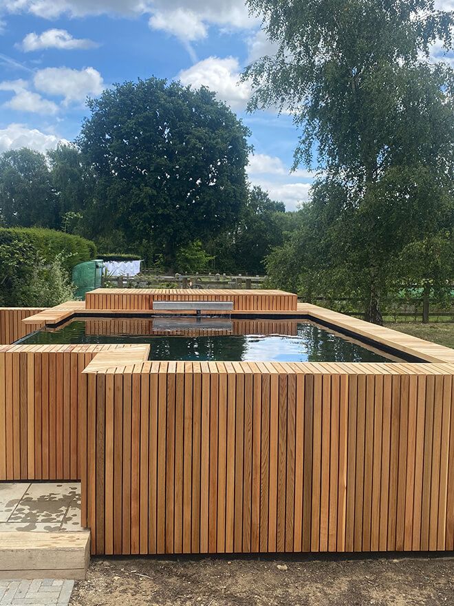 Raised timber-clad koi pond in a garden with trees behind