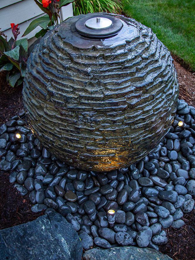 Lit slate sphere fountain on a bed of black pebbles